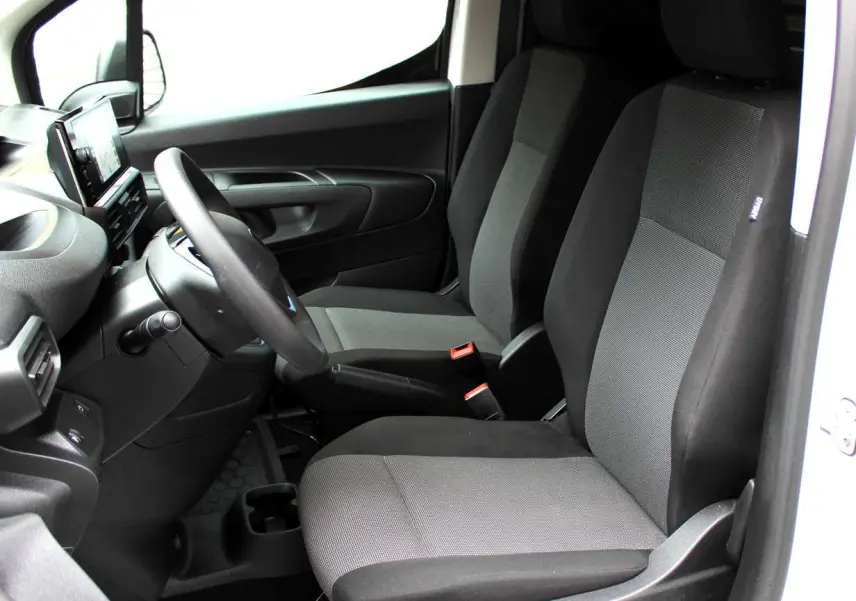 Vue intérieure côté conducteur du Peugeot Partner Fourgon 2025, sièges tissu gris et noir, tableau de bord moderne noir.