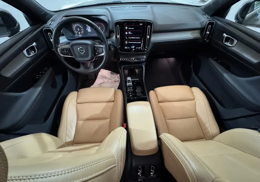 Vue intérieure avant du Volvo XC40 Recharge T5 2021 avec sièges cuir beige et tableau de bord noir moderne.