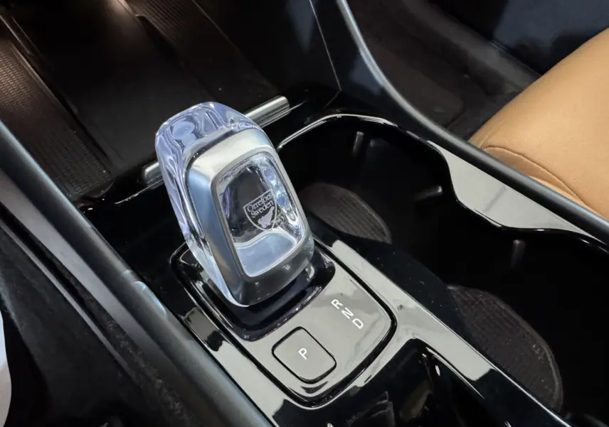 Gros plan sur la console centrale noire du Volvo XC40 Recharge T5 avec levier de vitesses en cristal Orrefors et siège cuir beige visible.