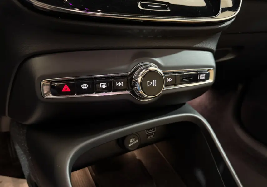 Gros plan sur la console centrale noire du Volvo XC40 Recharge T5 2021, avec commandes audio et prise 12V visibles.