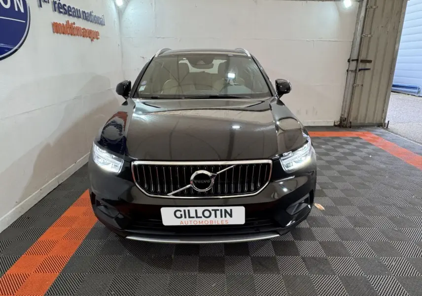 Vue frontale d'un Volvo XC40 noir hybride rechargeable avec phares LED allumés dans un showroom.