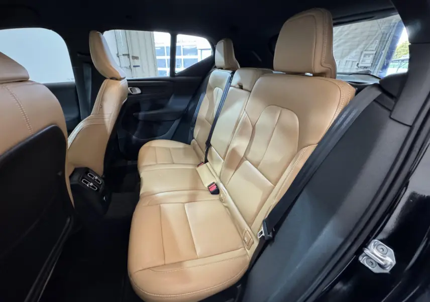 Vue intérieure côté droit des sièges arrière en cuir beige du Volvo XC40 noir, avec ceinture de sécurité et porte ouverte.