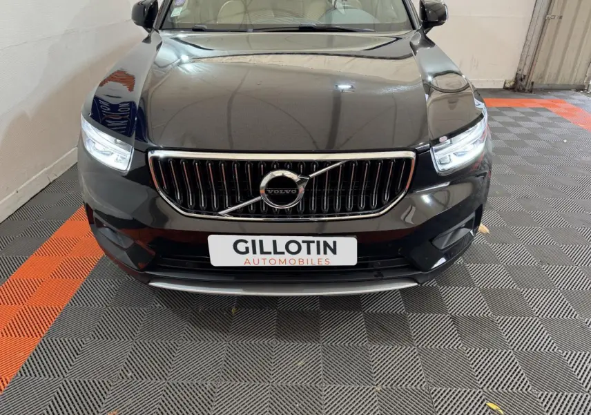 Vue avant d'un Volvo XC40 noir avec calandre chromée et phares LED allumés sur sol damier gris et orange.