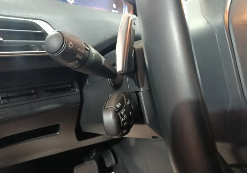 Gros plan sur la colonne de direction et commandes derrière le volant cuir noir d’un Peugeot 3008 marron, tableau de bord partiel visible.
