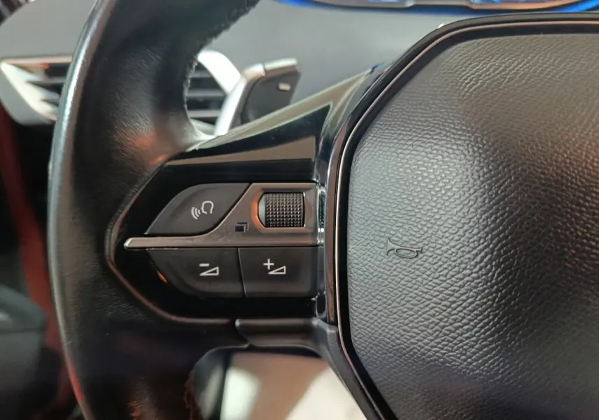 Gros plan sur le volant cuir noir du Peugeot 3008 2019, avec commandes audio et bouton klaxon visible.