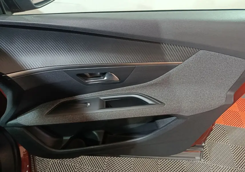 Vue intérieure du panneau de porte côté conducteur du Peugeot 3008 marron, avec insert imitation carbone et commande de vitre.