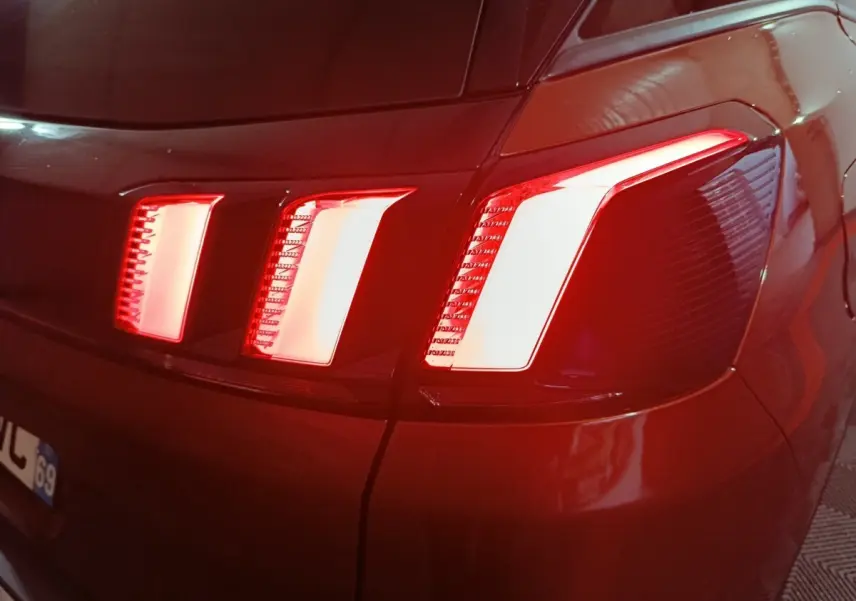 Gros plan sur le feu arrière droit rouge et blanc d’un Peugeot 3008 marron, vue arrière en faible lumière.