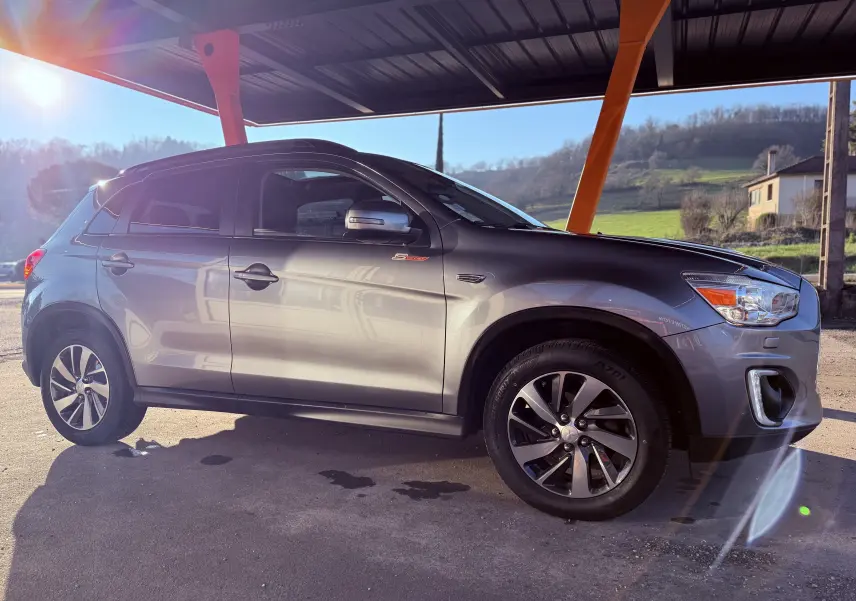 Mitsubishi ASX gris vu de profil côté gauche, sous un abri avec lumière du soleil en arrière-plan.