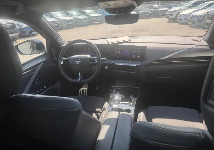 Vue intérieure avant de l’Opel Astra 2024 noire, montrant le volant cuir, l’écran tactile large et l’accoudoir central.