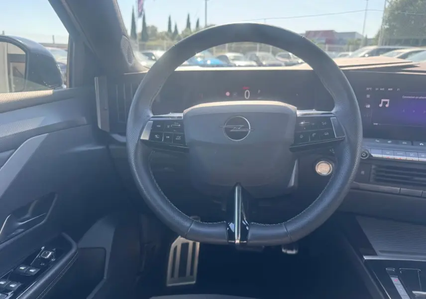 Vue intérieure centrée sur le volant cuir noir de l'Opel Astra 2024 avec commandes intégrées et tableau de bord digital.