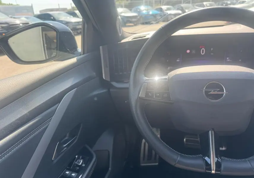 Vue intérieure côté conducteur de l'Opel Astra 2024 noire, volant cuir avec commandes intégrées et rétroviseur électrique.