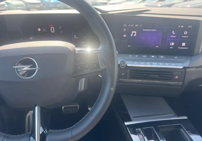 Vue rapprochée de l'intérieur de l'Opel Astra 2024, volant cuir noir avec commandes et écran tactile central lumineux.
