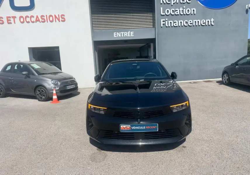 Vue frontale d'une Opel Astra noire 2024 avec feux LED allumés, stationnée devant un bâtiment commercial.