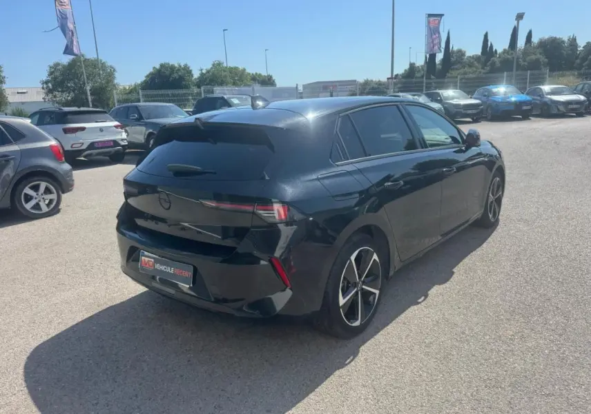 Opel Astra noir vue 3/4 arrière droit, vitres surteintées et jantes alliage 17 pouces visibles en extérieur.