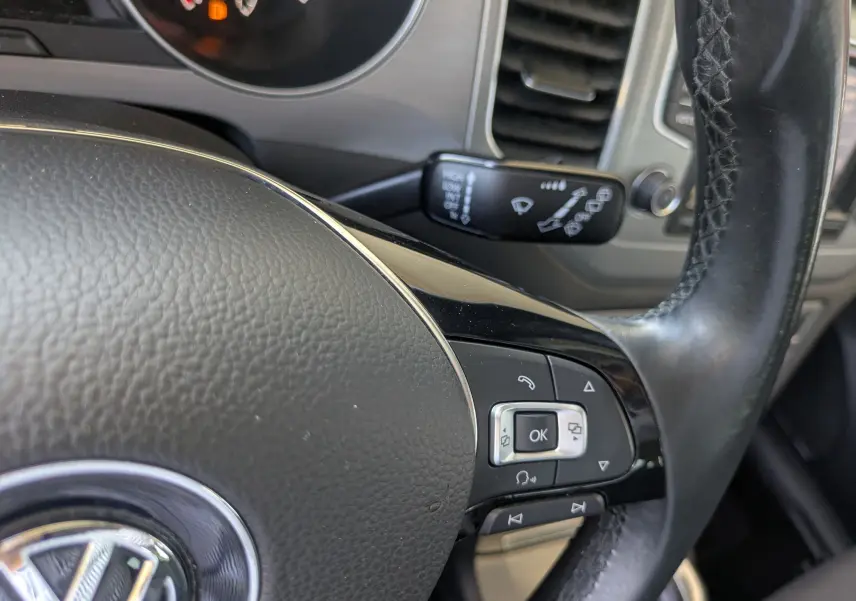 Gros plan sur le volant en cuir noir de la Volkswagen Golf Sportsvan 2014, avec commandes intégrées et tableau de bord partiel.