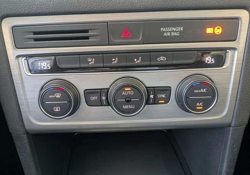 Vue rapprochée de la console centrale argentée du Volkswagen Golf Sportsvan noir, avec commandes de climatisation digitales.