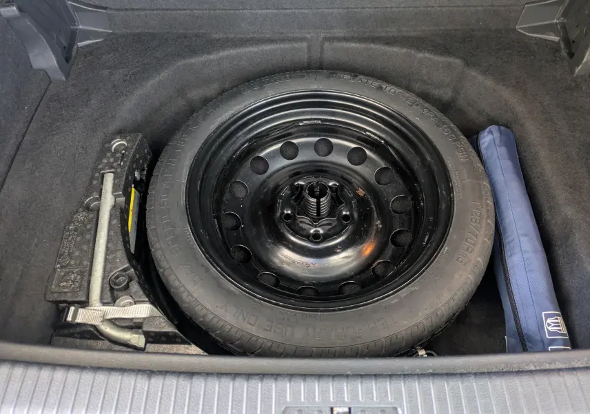 Vue plongeante sur la roue de secours noire et les outils dans le coffre d'une Volkswagen Golf Sportsvan noire.