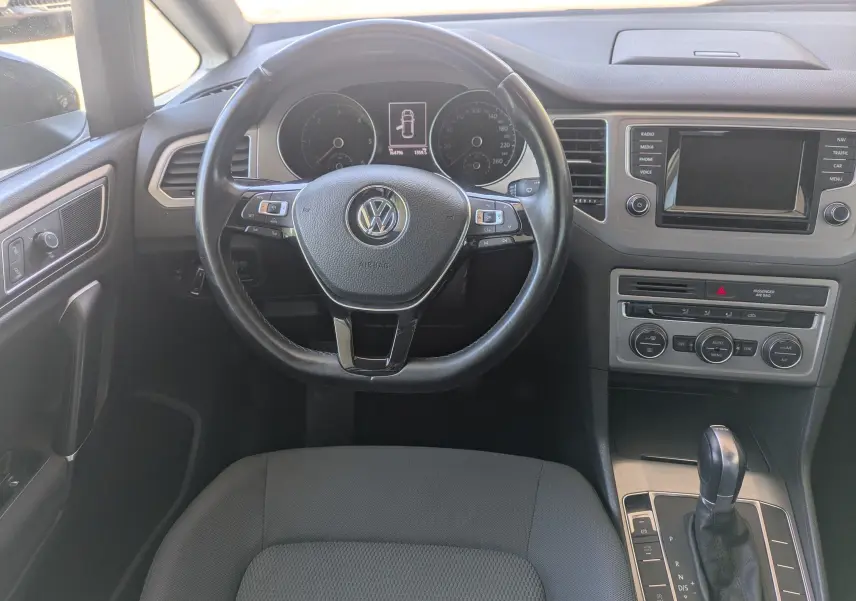 Vue intérieure centrée sur le volant noir d'une Volkswagen Golf Sportsvan Confortline 2014 avec console et levier de boîte auto.