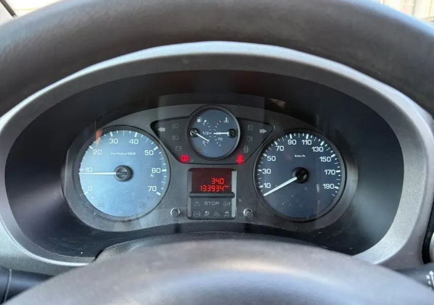 Vue rapprochée du tableau de bord du Peugeot Partner Tepee rouge, affichant compteurs et indicateurs derrière le volant.