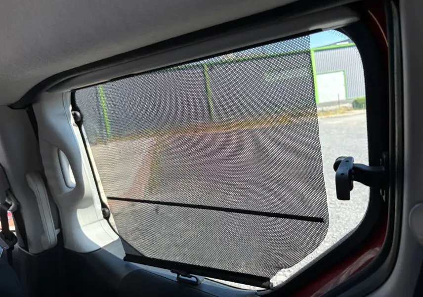Vue intérieure sur le rideau pare-soleil du côté gauche d’un Peugeot Partner Tepee rouge de 2016.