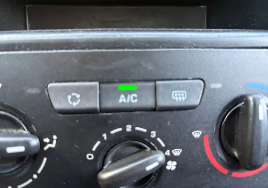 Gros plan sur le tableau de bord du Peugeot Partner Tepee rouge, mettant en valeur la commande de climatisation manuelle avec bouton A/C allumé.