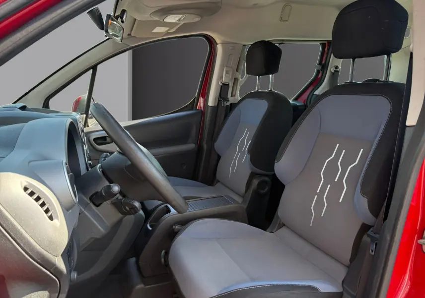 Vue intérieure côté conducteur du Peugeot Partner Tepee rouge 2016, sièges avant gris avec motifs blancs et volant réglable.