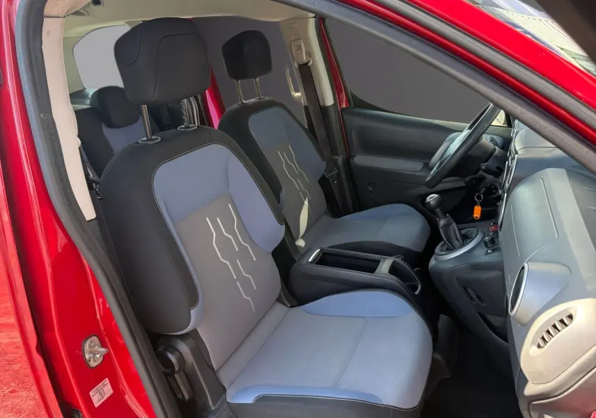 Vue intérieure côté gauche du Peugeot Partner Tepee rouge 2016, montrant sièges avant bi-ton et volant réglable.