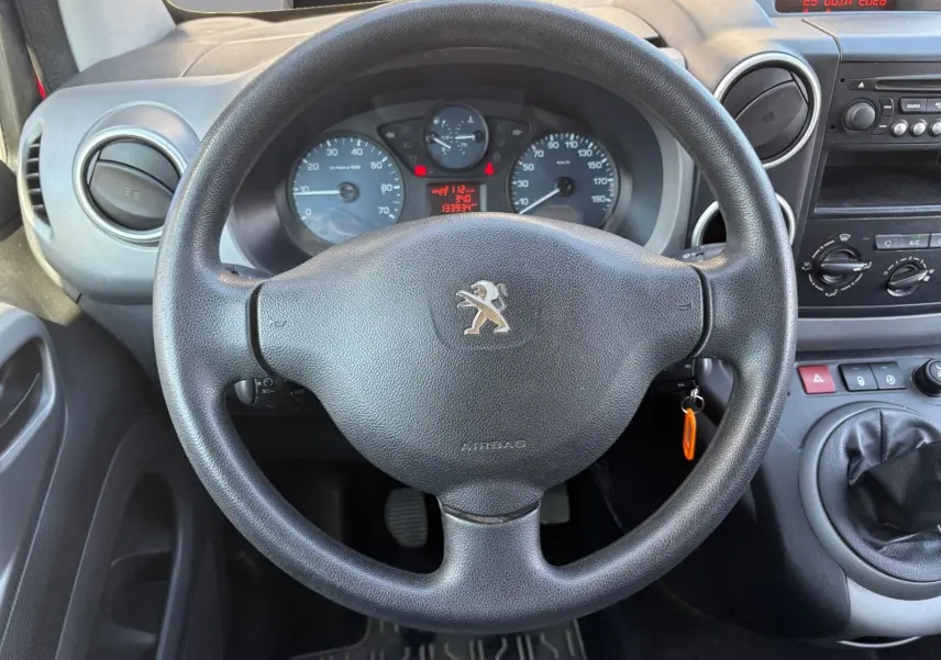 Vue intérieure centrée sur le volant Peugeot noir, tableau de bord et levier de vitesses d’un Partner Tepee rouge de 2016.