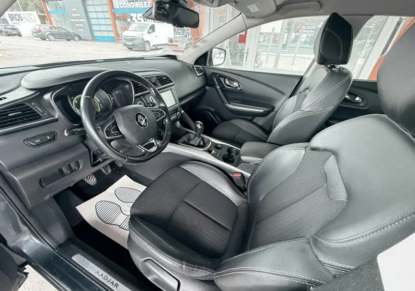 Vue intérieure côté conducteur du Renault Kadjar gris 2016, montrant les sièges en tissu et cuir ainsi que le tableau de bord.