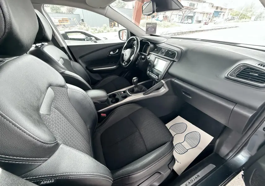Vue intérieure côté passager du Renault Kadjar gris, montrant sièges en cuir et tissu et tableau de bord moderne.
