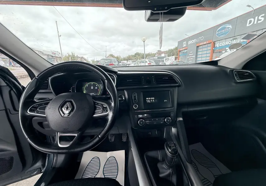 Vue intérieure avant du Renault Kadjar gris, montrant le volant, tableau de bord et levier de vitesses manuel.