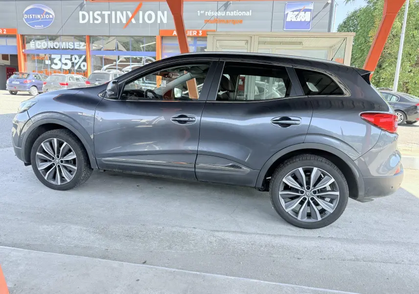 Profil côté gauche d'un Renault Kadjar gris 2016 garé sous un abri avec jantes alliage et vitres teintées.