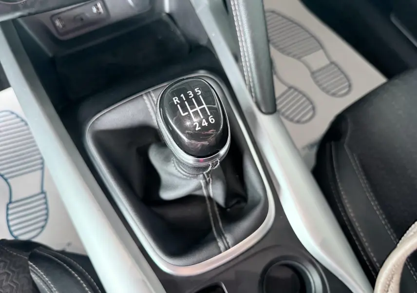 Gros plan sur la commande de la boîte manuelle noire du Renault Kadjar gris, avec coutures blanches visibles autour.