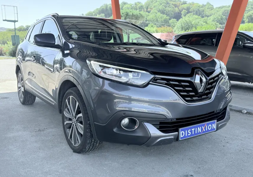 Renault Kadjar gris en 3/4 avant droit, avec calandre noire et jantes alliage visibles sous abri.