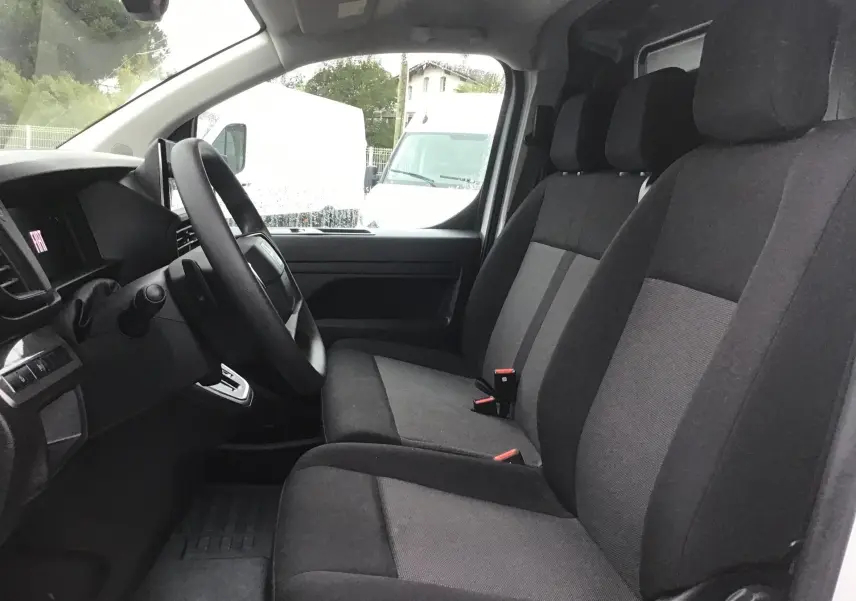Vue intérieure côté conducteur du Fiat Scudo Fourgon blanc 2024, sièges tissu gris et tableau de bord simple.