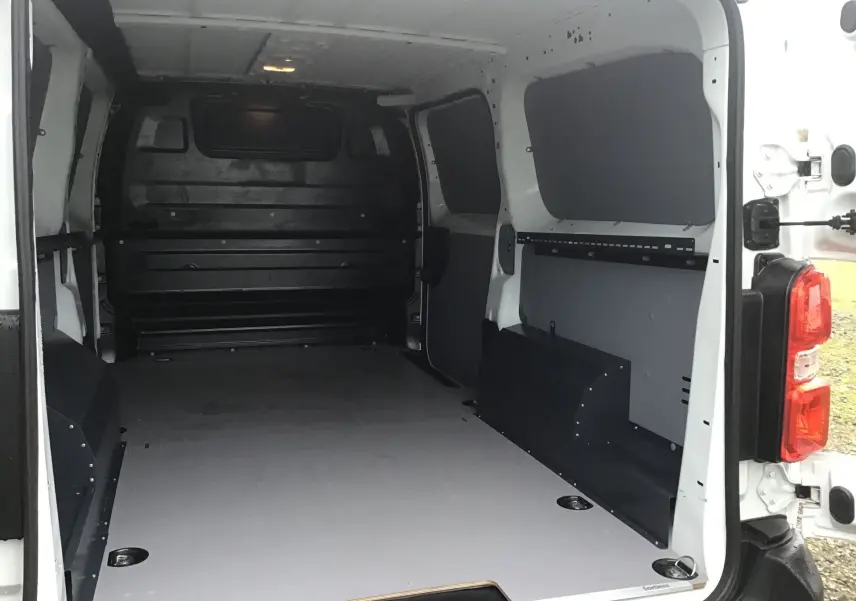 Vue intérieure arrière du fourgon FIAT Scudo XL blanc 2024, montrant l’espace de chargement avec revêtement PVC et protections latérales noires.