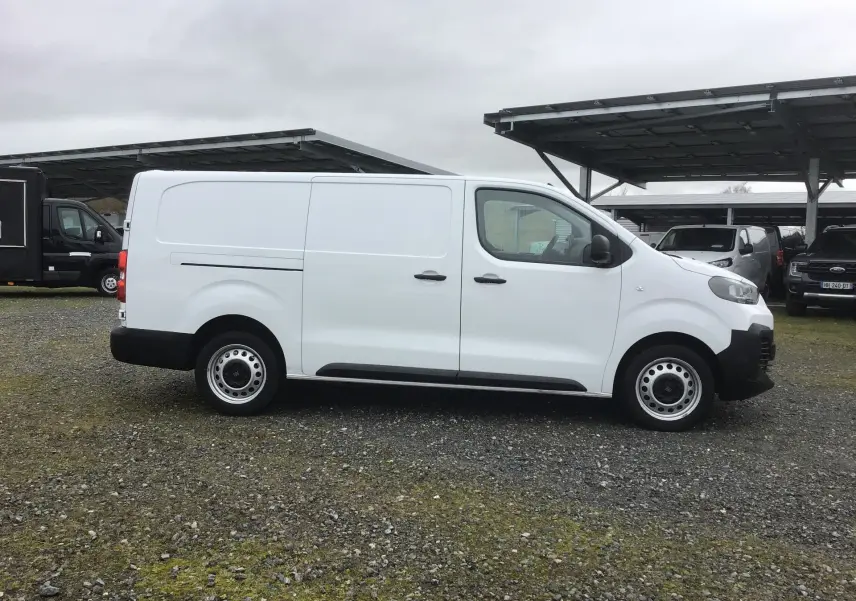 Vue de profil côté droit d’un FIAT Scudo Fourgon blanc 2024 avec porte latérale coulissante, stationné sur sol gravillonné.