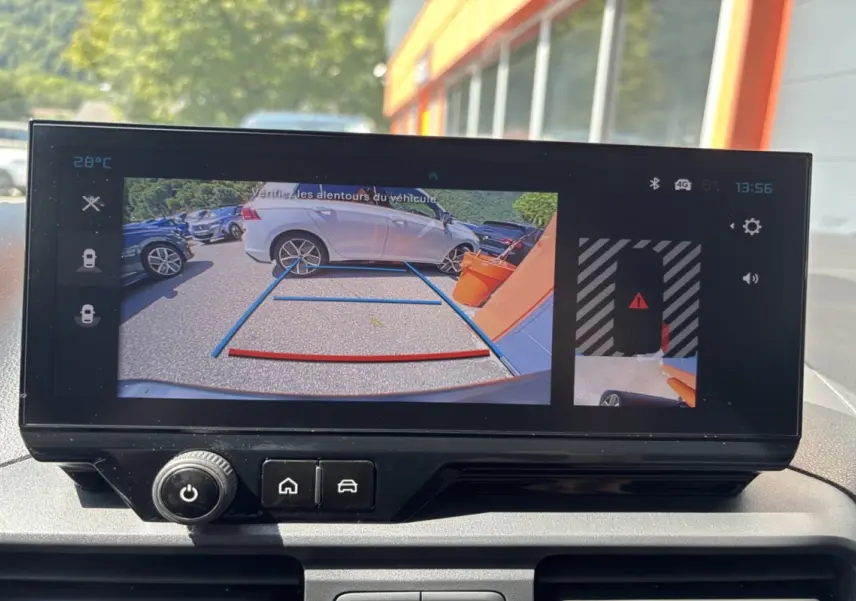 Écran de caméra de recul montrant une voiture grise en 3/4 arrière droite près d’un mur orange.