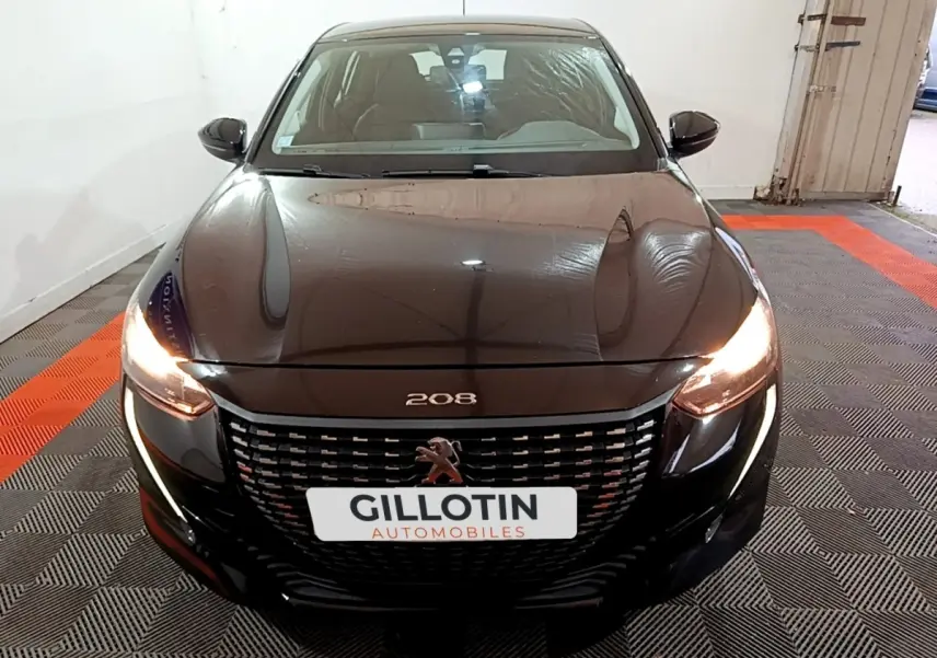 Vue avant d'une Peugeot 208 noire de 2020 avec phares allumés et calandre au lion distinctif.