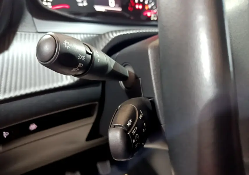 Gros plan sur les commandes au volant noir d’un Peugeot 208 2020, avec tableau de bord numérique en arrière-plan flou.