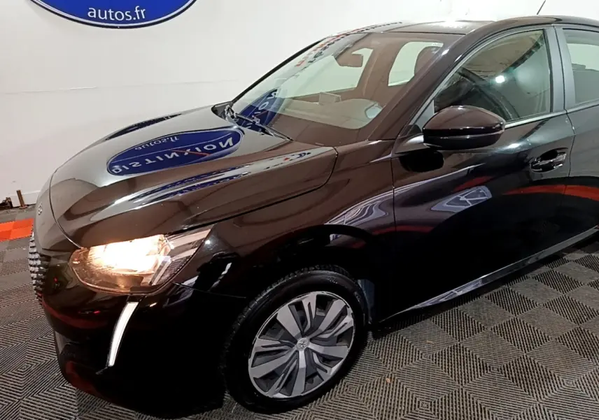 Vue 3/4 avant droit d'une Peugeot 208 noire avec phares allumés et jantes distinctives en intérieur showroom.