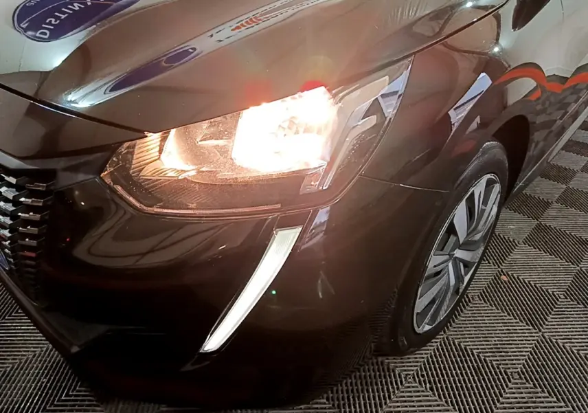 Gros plan sur l'avant droit noir d'une Peugeot 208 2020 avec phare allumé et feux diurnes en forme de griffes.