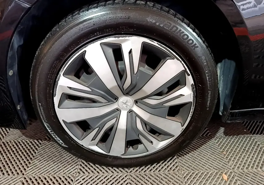 Gros plan sur la roue avant droite d’une Peugeot 208 noire, mettant en valeur la jante aluminium au design moderne.