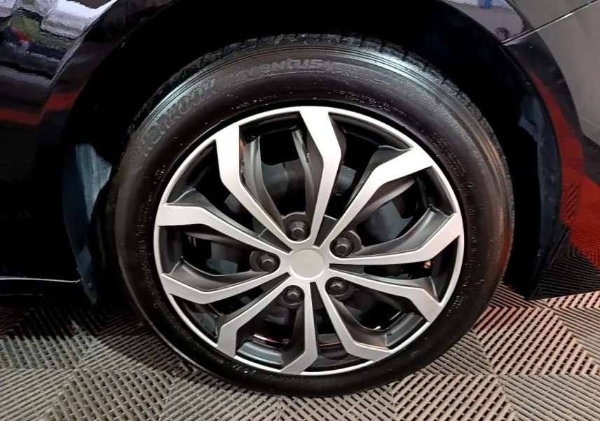 Gros plan sur la roue avant droite d'une Peugeot 208 noire, mettant en valeur la jante alliage au design moderne.