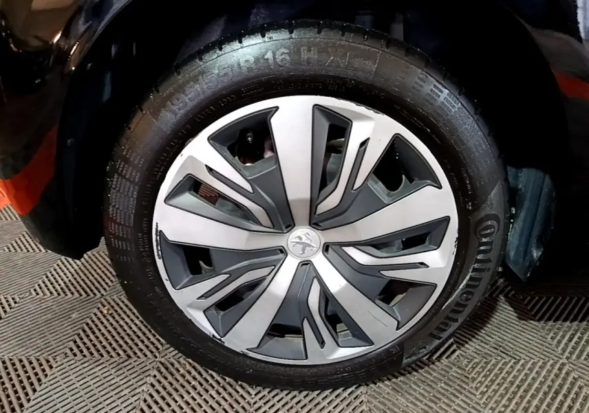 Gros plan sur la roue avant gauche d’une Peugeot 208 noire, avec jante alliage au design moderne bicolore.