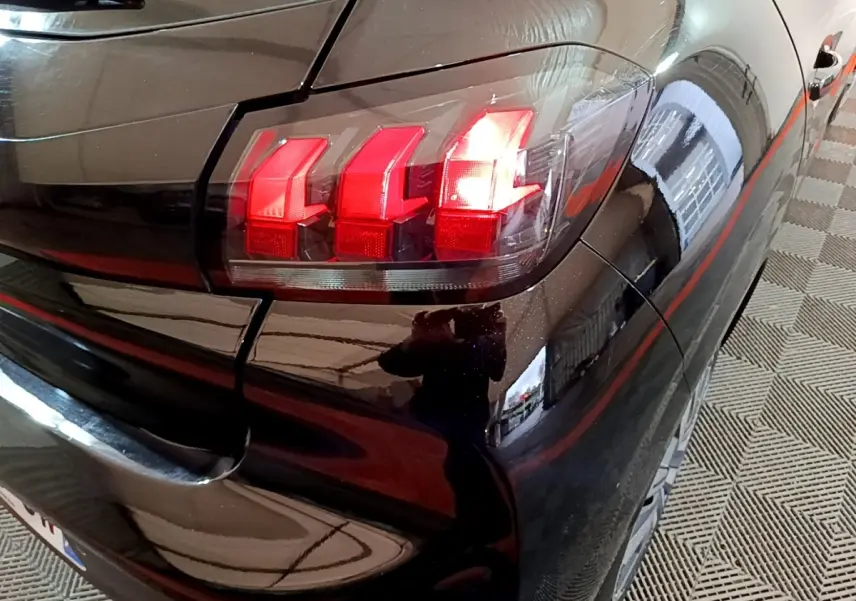 Gros plan sur le feu arrière droit rouge d'une Peugeot 208 noire, vue depuis l'arrière côté droit.