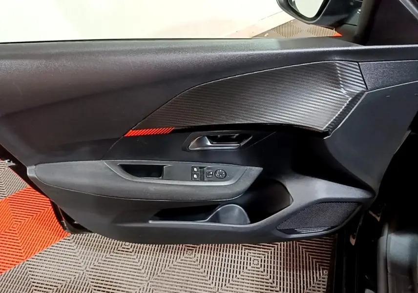 Gros plan sur la porte intérieure côté conducteur de la Peugeot 208 noire, avec commandes électriques et finition effet carbone.