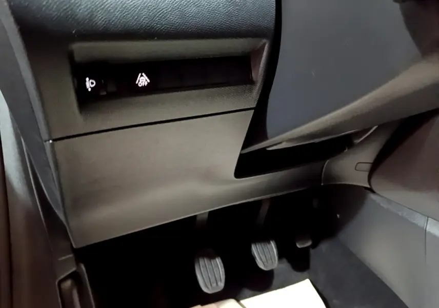 Vue rapprochée du côté gauche sous le tableau de bord noir de la Peugeot 208 avec pédales manuelles et commandes éclairées.