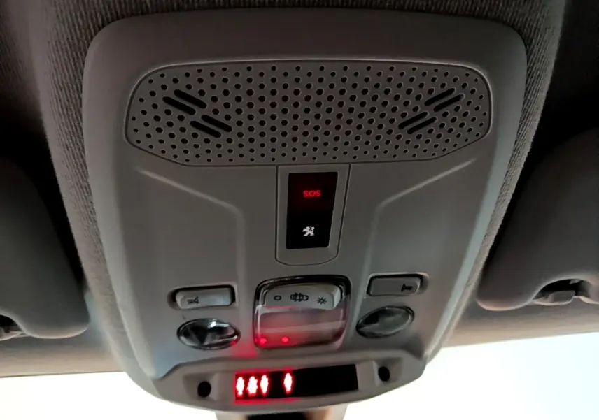 Vue en gros plan du panneau de commande intérieur au plafond de la Peugeot 208 noire, avec bouton SOS rouge allumé.