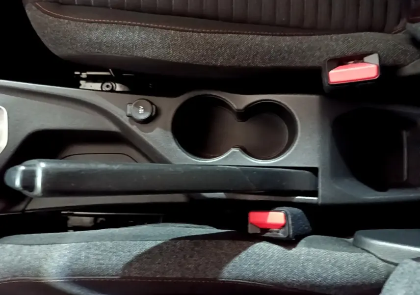 Vue plongeante sur la console centrale noire de la Peugeot 208 avec frein à main manuel et deux porte-gobelets.